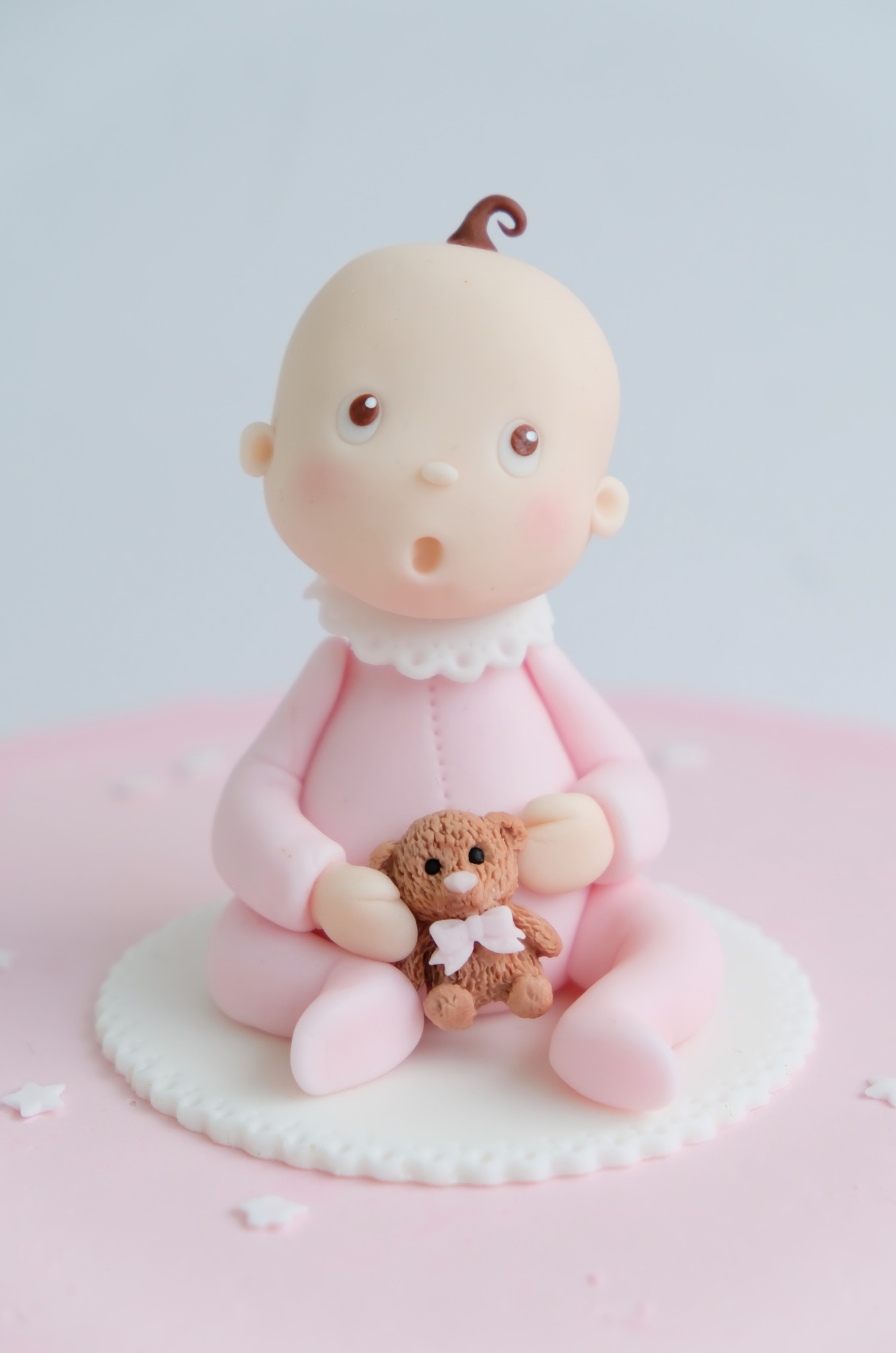Una figura de bebé con un traje rosa sostiene un osito de peluche.