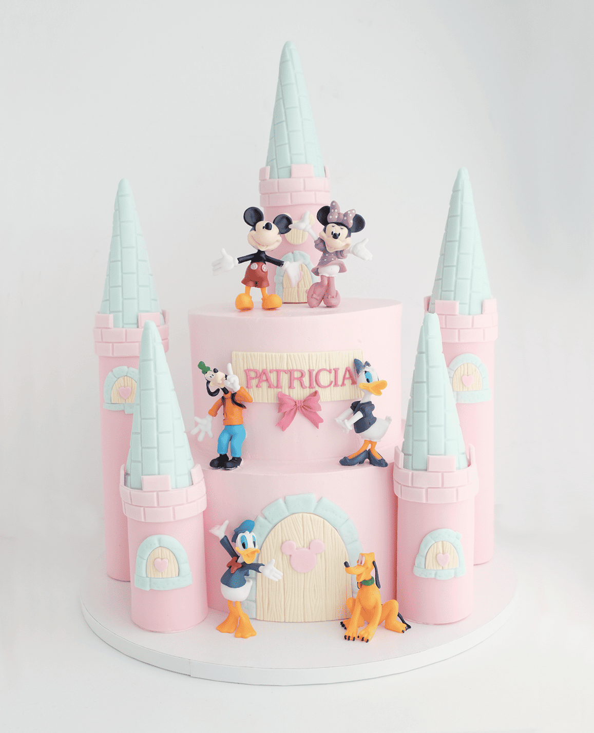 Un pastel de castillo rosa con Mickey Mouse y Minnie Mouse encima.