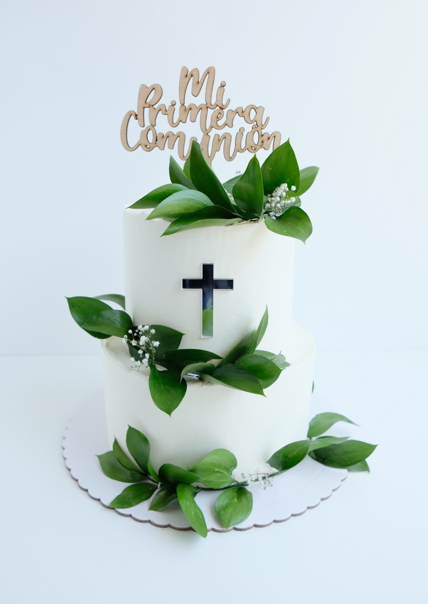 Un pastel blanco con hojas verdes y una cruz en la parte superior.