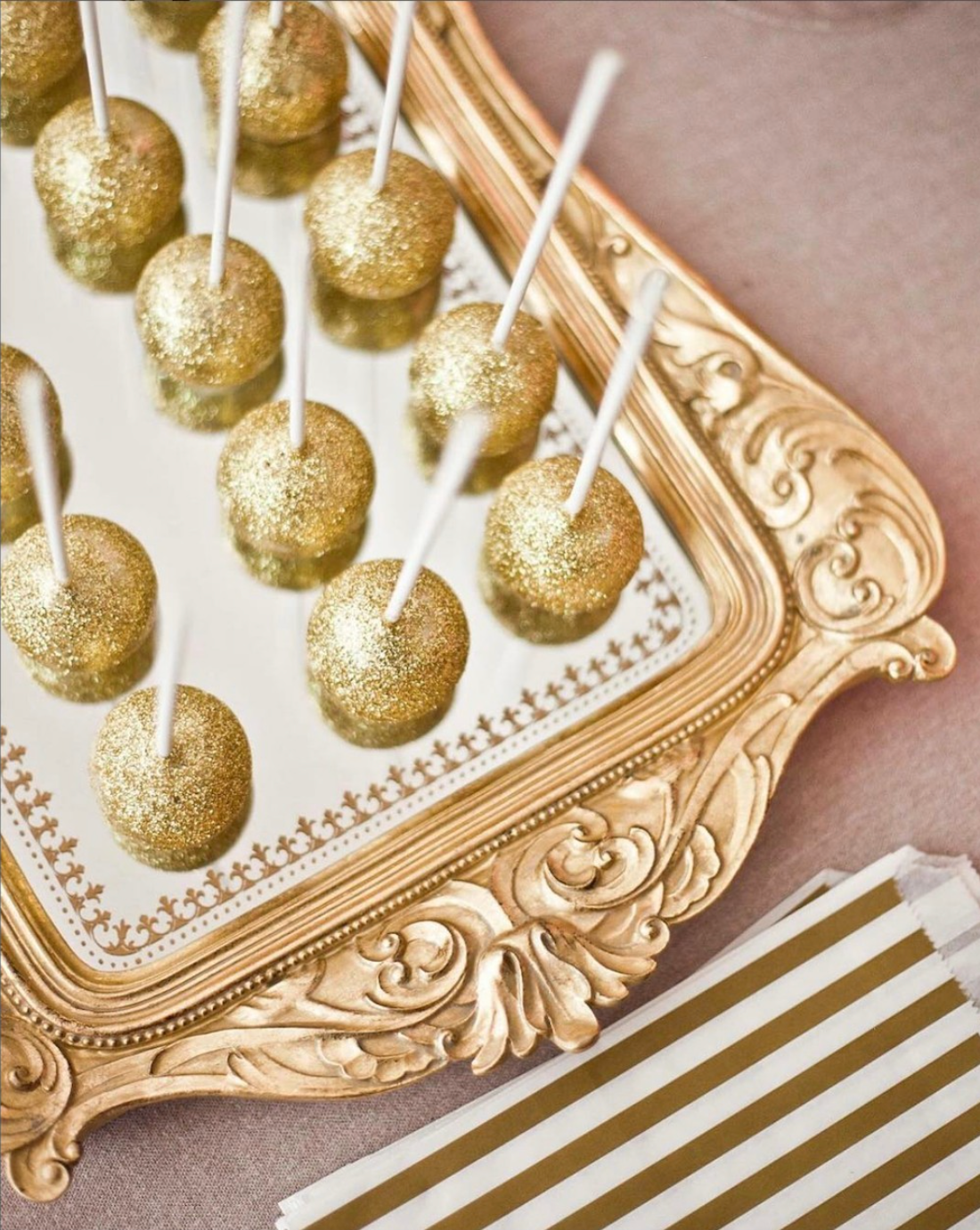 Una bandeja de oro llena de cake pops dorados en palitos