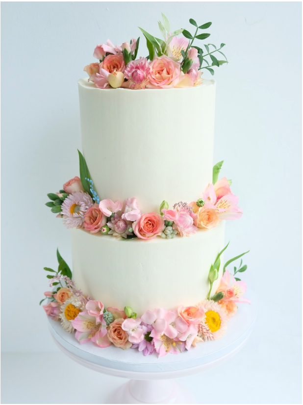 Un pastel blanco con flores rosas y naranjas encima.