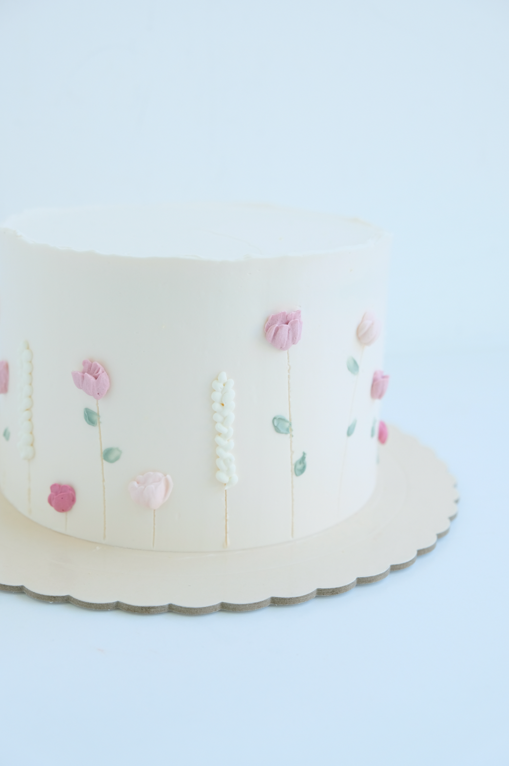 Un pastel blanco con flores rosas encima está sobre un plato blanco.