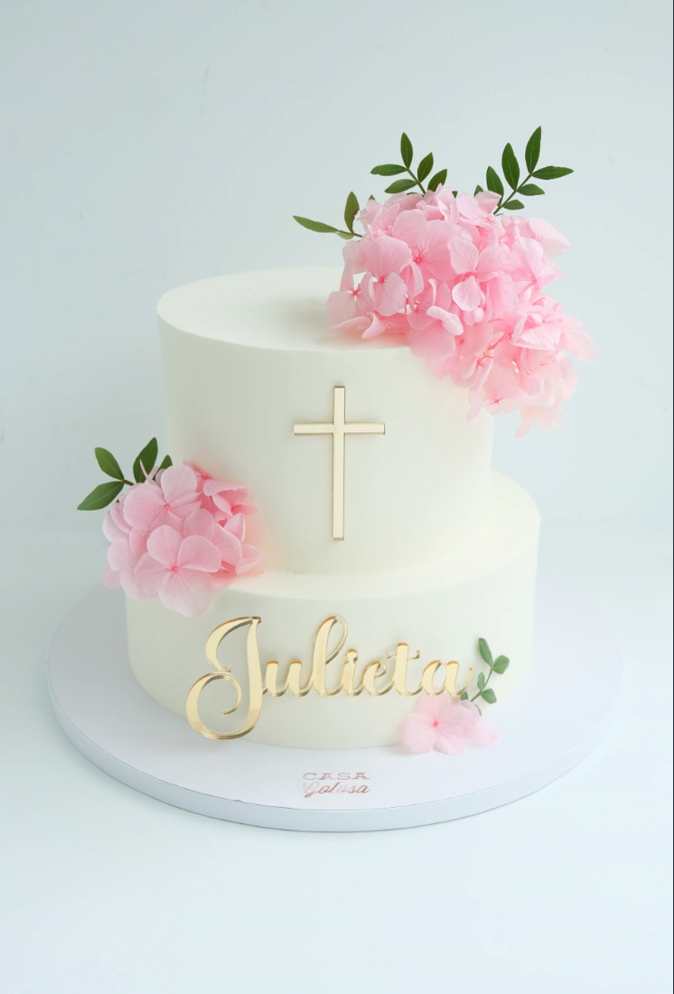 Un pastel blanco con una cruz y flores rosas en la parte superior. y nombre julieta