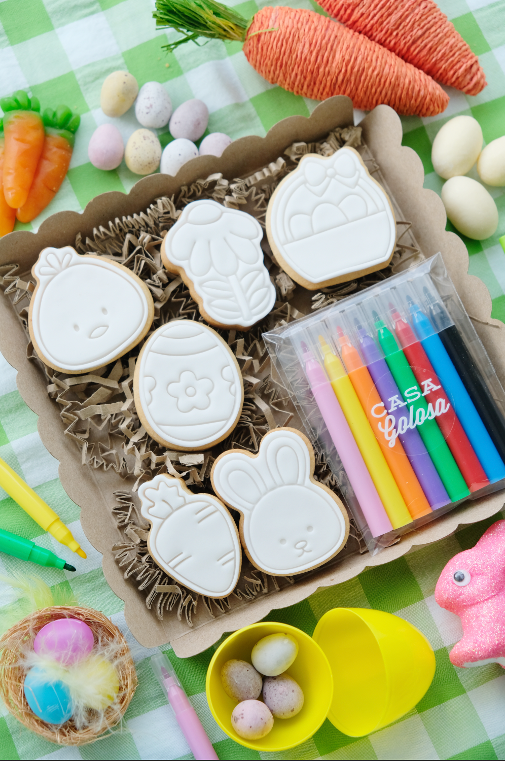 Una caja de galletas de Pascua con marcadores y zanahorias sobre una mesa.
