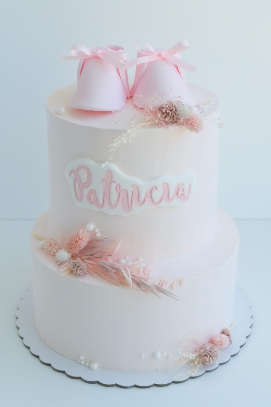 Un pastel blanco con zapatitos de bebé rosas encima.