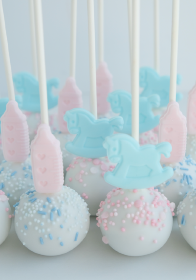Un montón de cake pops con caballitos de madera sobre una mesa.