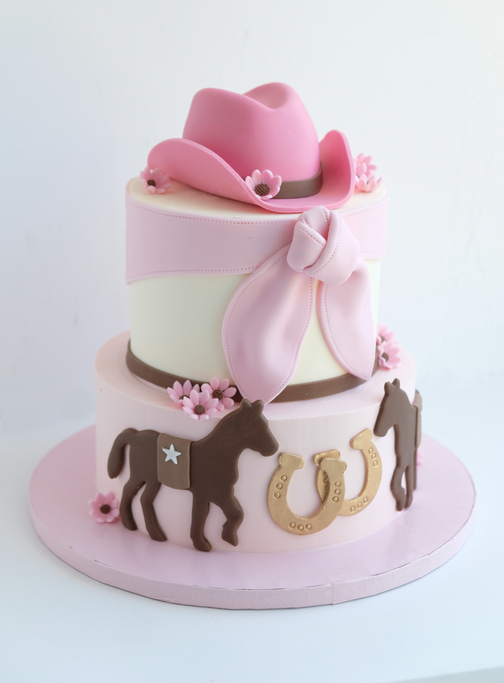 Un pastel rosa con un sombrero de vaquero y caballos encima.