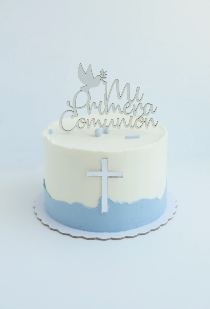 Un pastel con una cruz y un adorno que dice mi primera comunión.