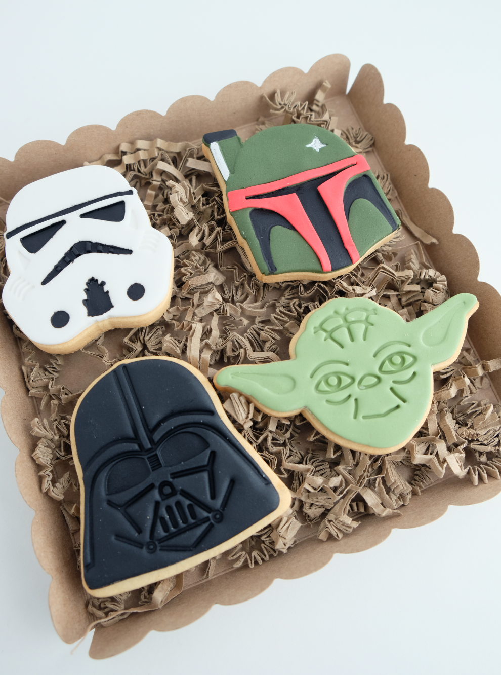 Cuatro galletas de Star Wars están en una caja encima de papel triturado.