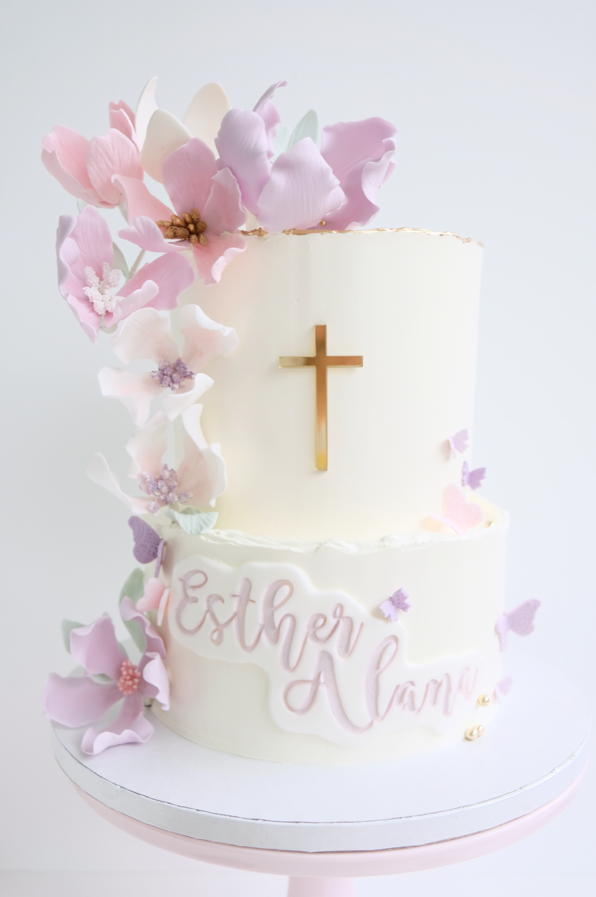 Un pastel blanco con flores y una cruz encima.