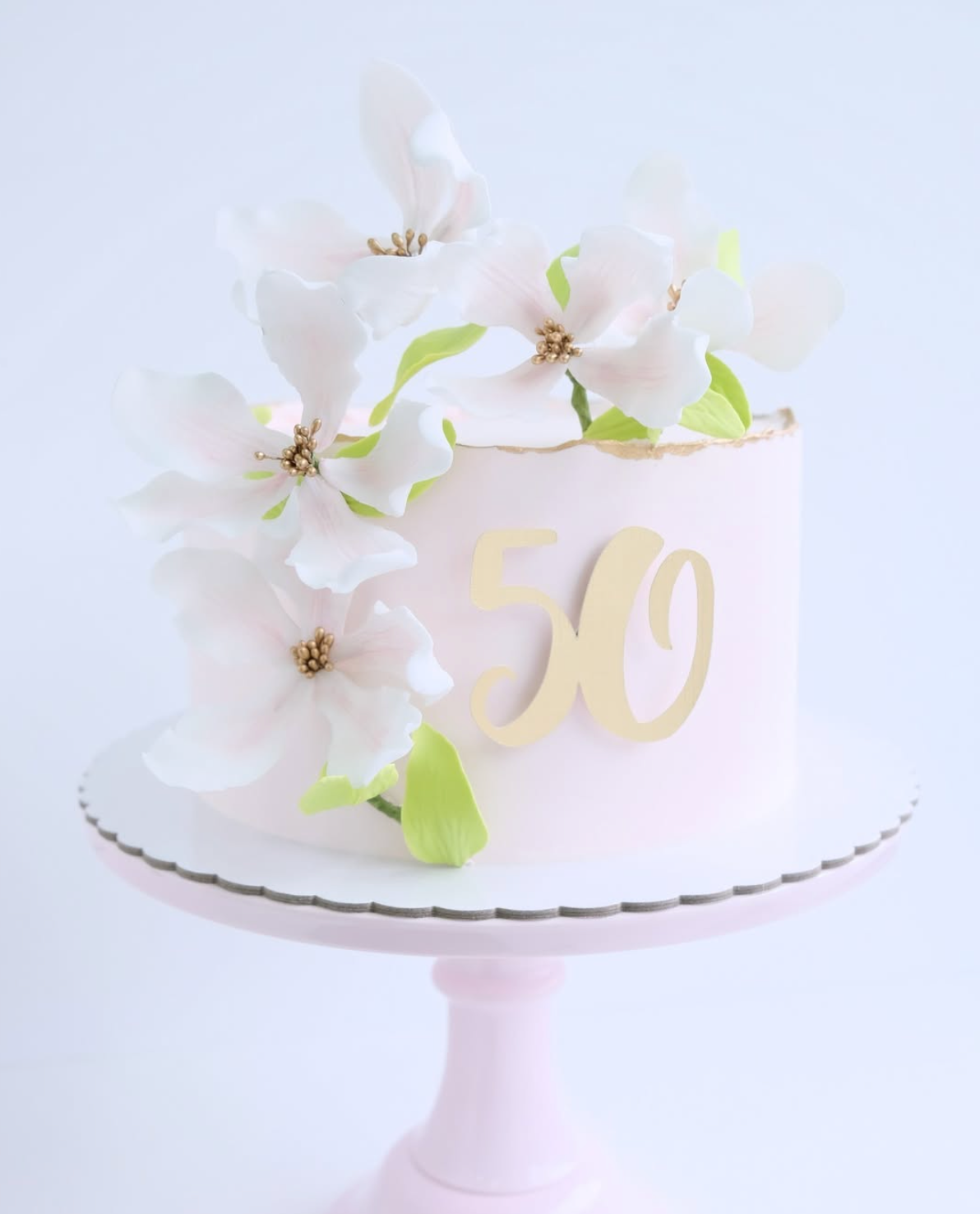 Un pastel rosa con flores blancas y el número 50 en él.