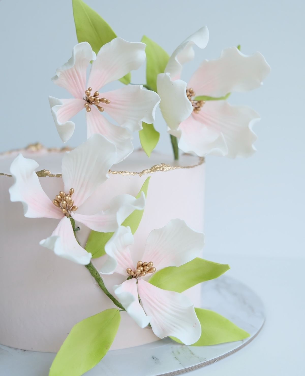 Un pastel rosa decorado con flores blancas y hojas verdes.