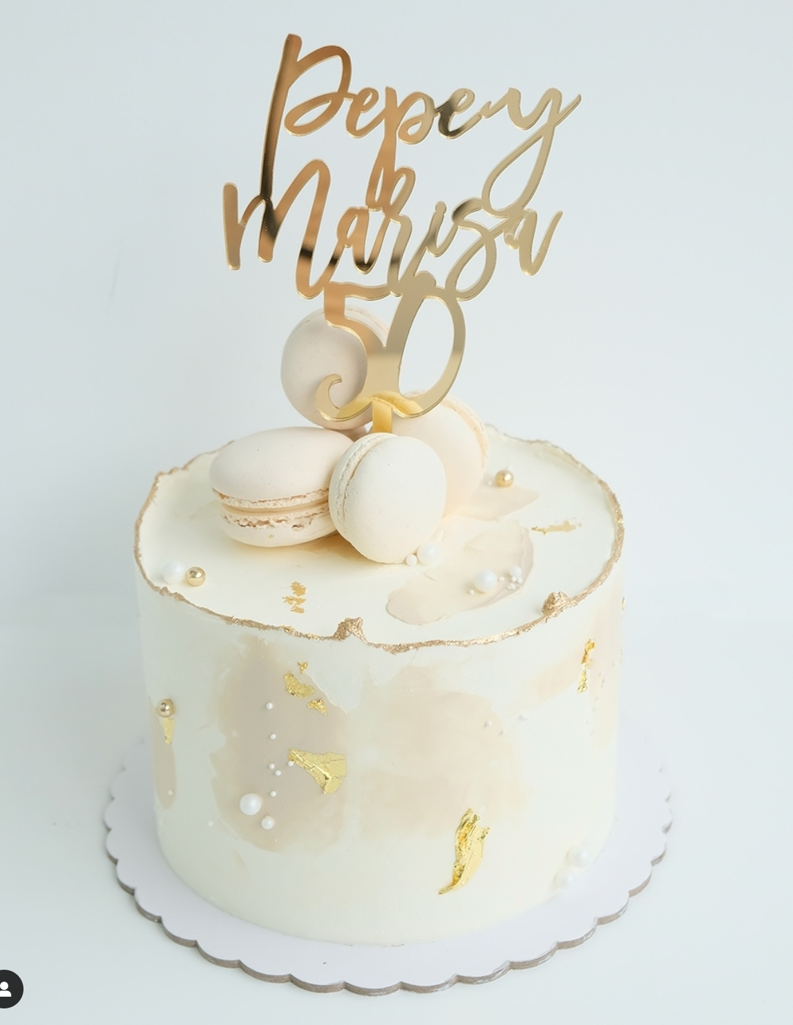 Un pastel blanco con macarons y un adorno dorado.