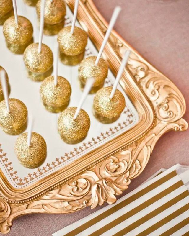 Una bandeja de oro llena de cake pops dorados en palitos