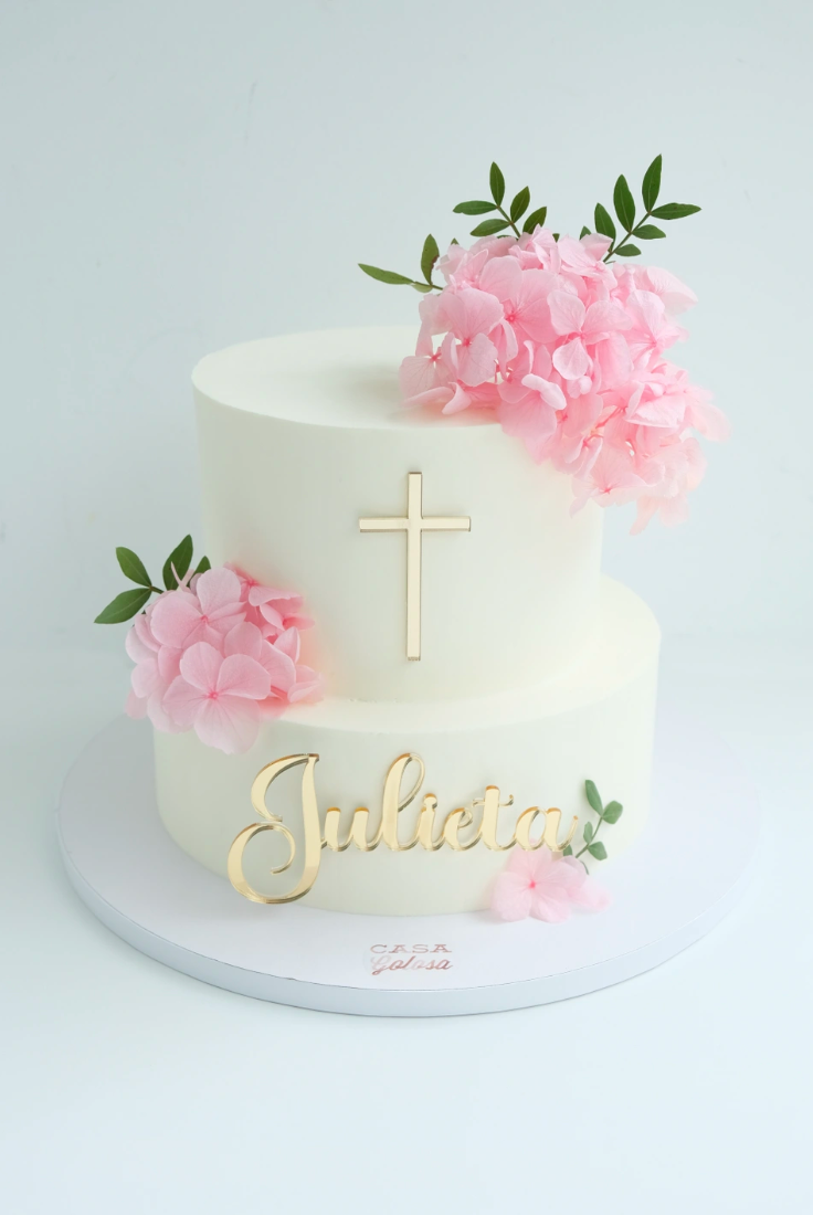 Un pastel blanco con una cruz y flores rosas en la parte superior.