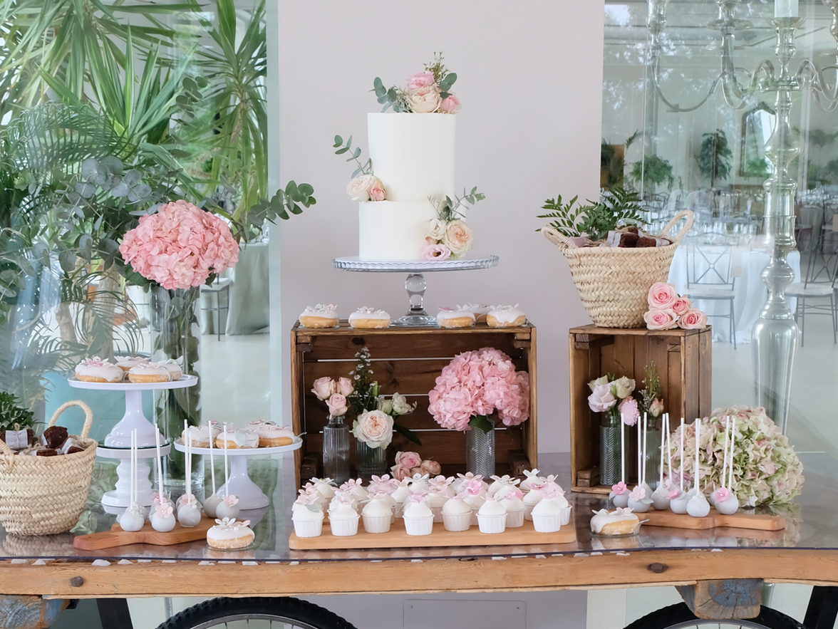 Una mesa con un pastel, pastelitos y flores.