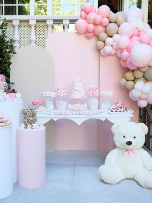 Mesa decorada con globlos rosados, blancos y dorados , oso blanco y pasteles