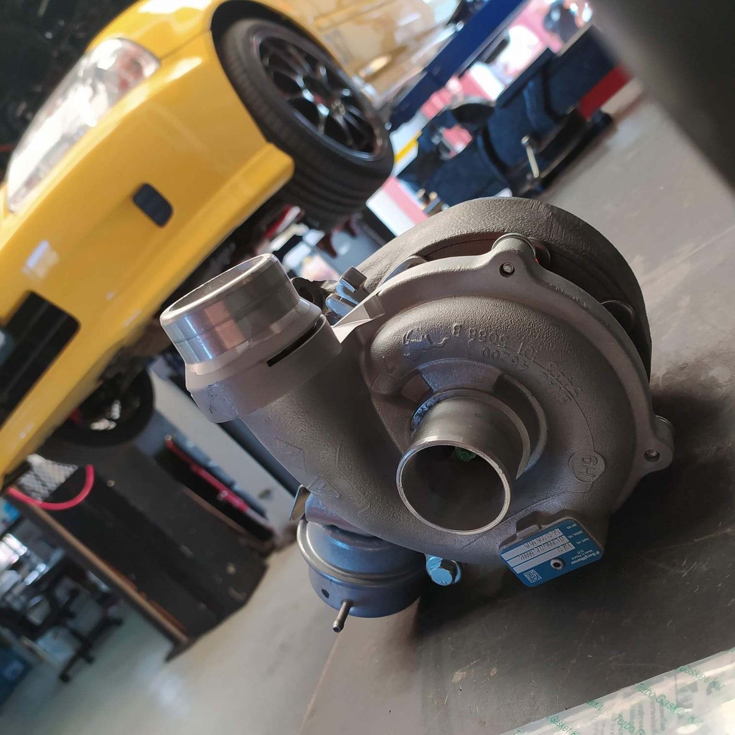 Un turbocompresor está sentado delante de un coche amarillo.