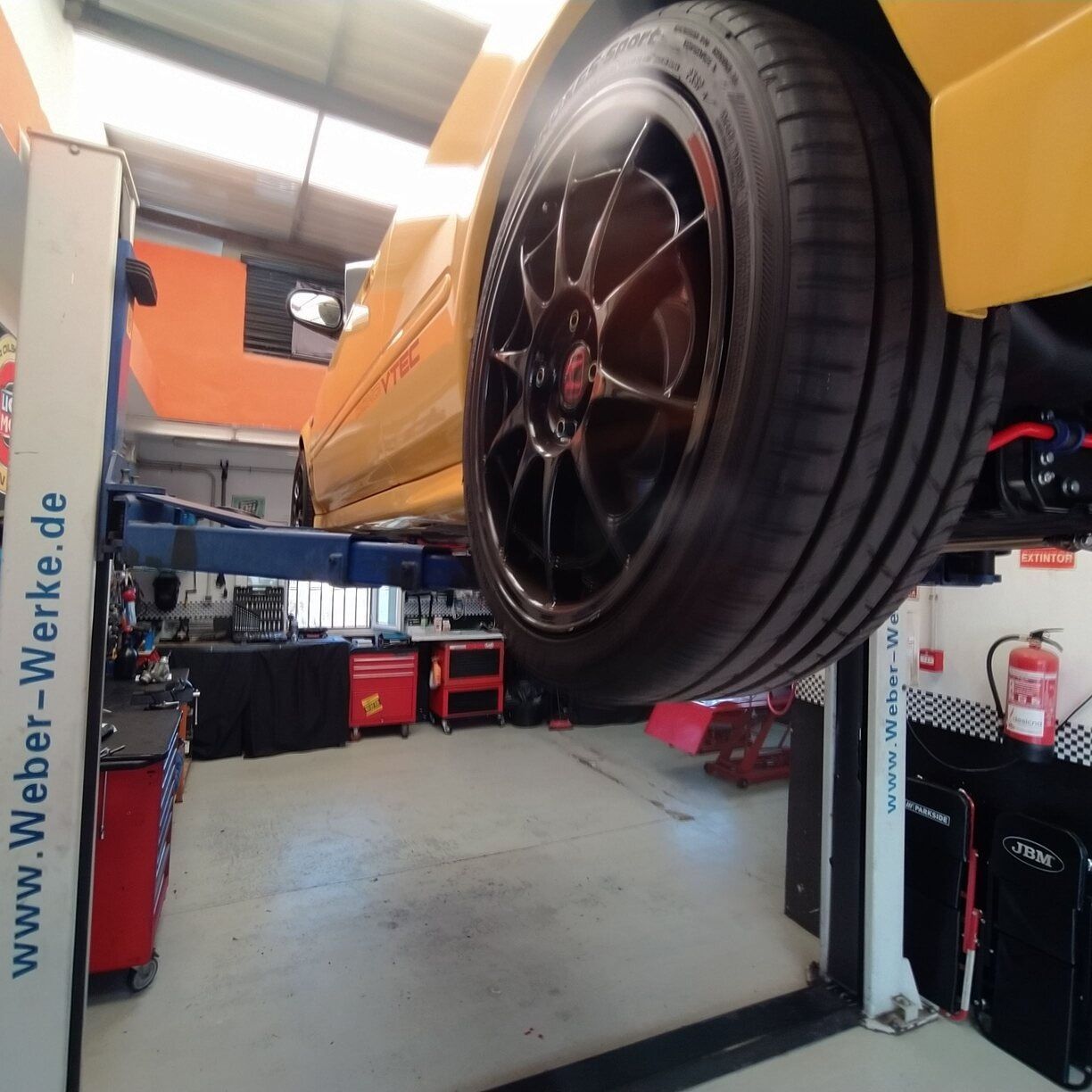 Un coche amarillo está en un ascensor en un garaje con un cartel que dice www.faber-werke.de