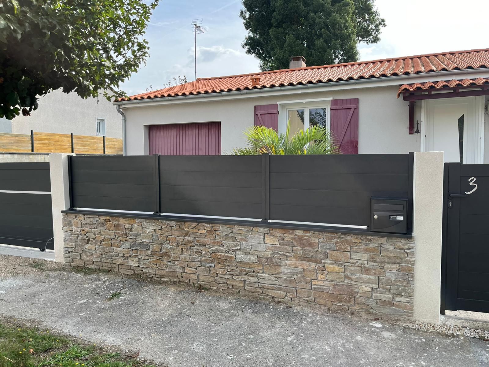 Clôture grise le long d'un muret en pierre