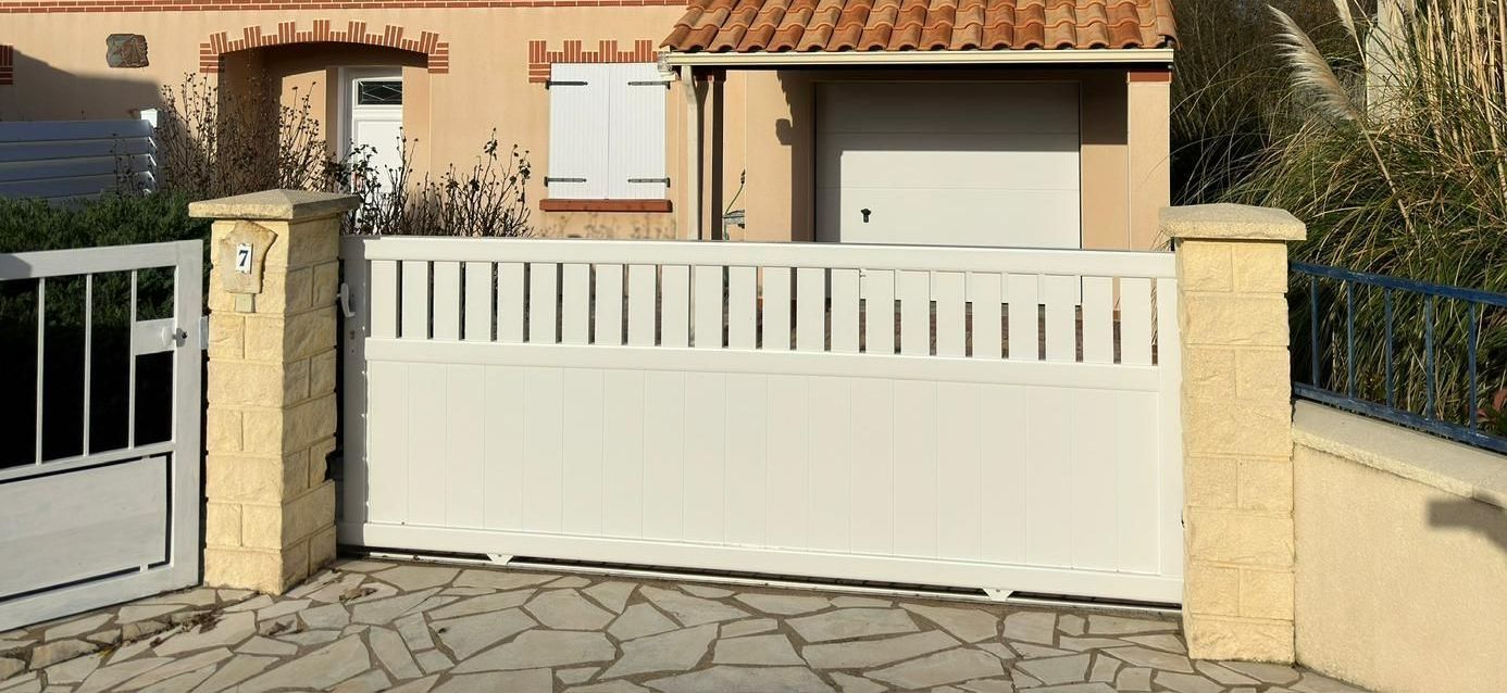 Un portail et son portillon de couleur blanc devant une maison aux murs en crépi
