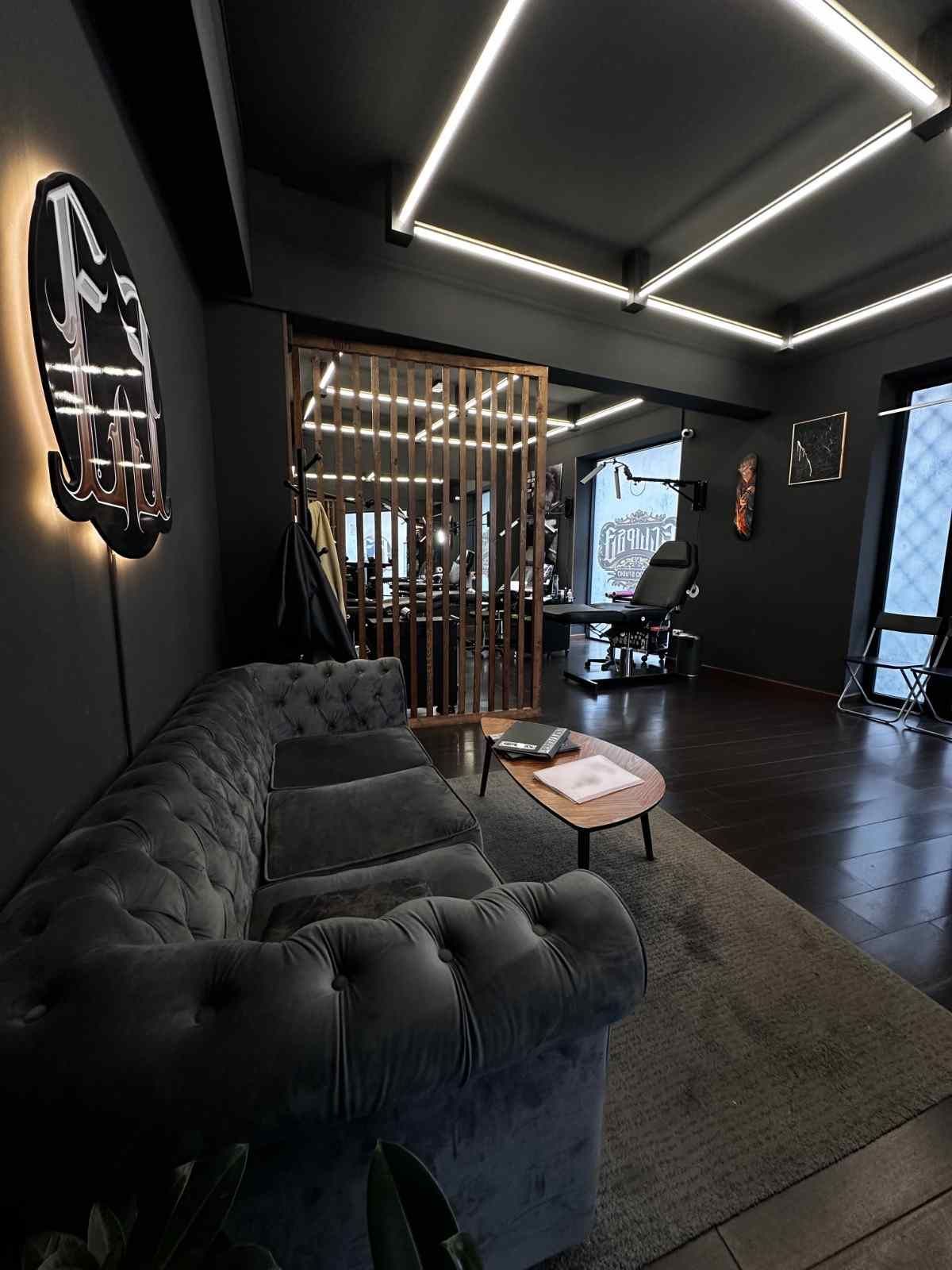 Salón moderno de color negro con sofá capitoné, lámparas de techo geométricas y una mampara de madera.