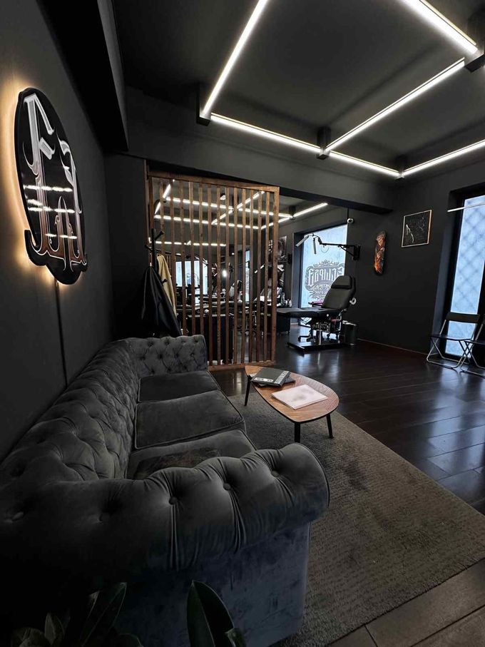 Salón moderno de color negro con sofá capitoné, lámparas de techo geométricas y una mampara de madera.