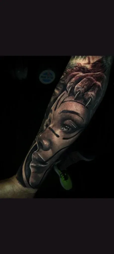Antebrazo tatuado con un detallado tatuaje monocromático de un rostro femenino sobre un fondo oscuro.