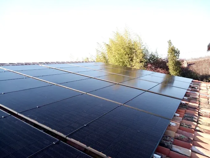 Des panneaux solaires installés sur un toit, à côté d'arbres, sous un ciel lumineux.