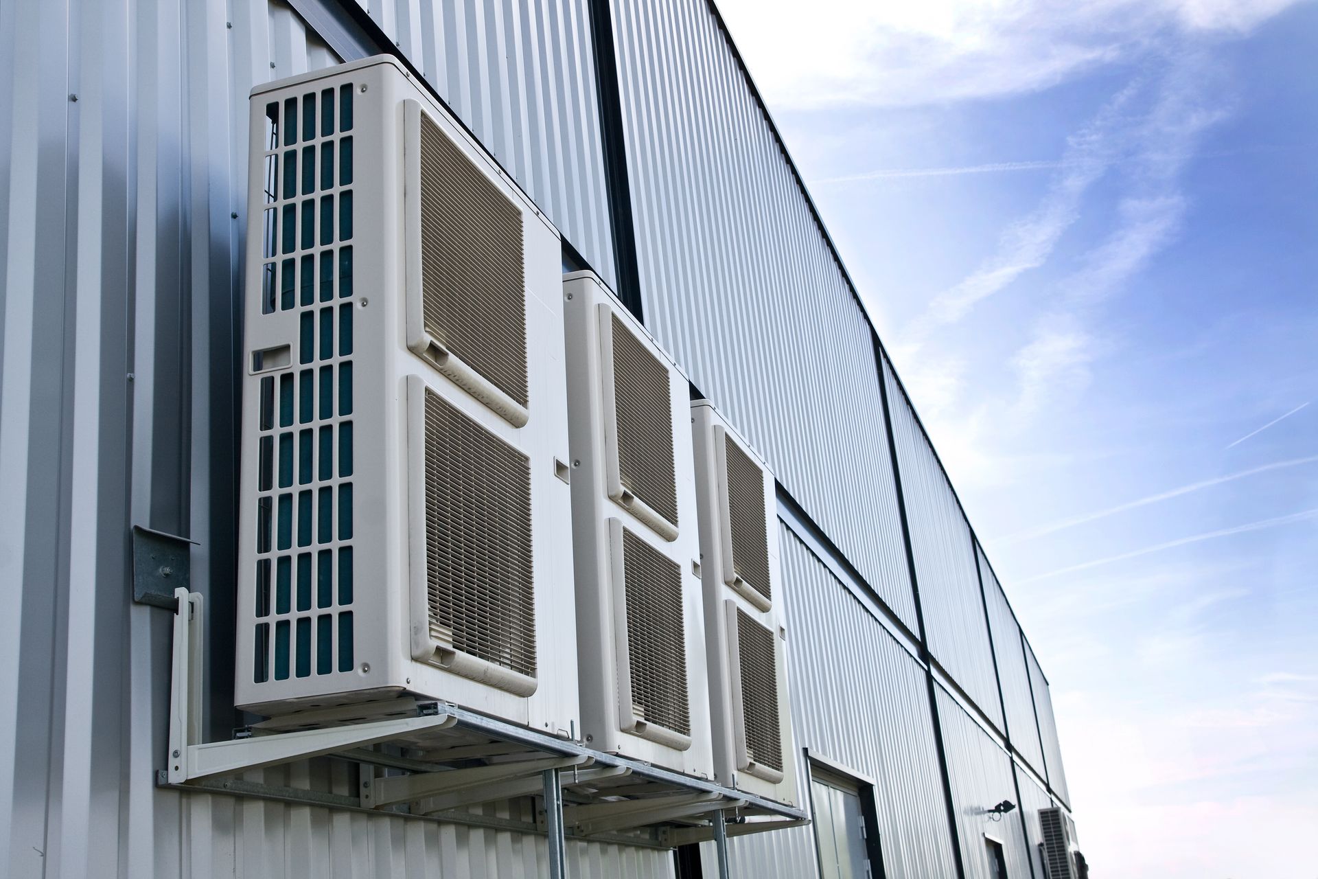 Rangée de climatiseurs de fenêtre installés sur un bâtiment en tôle ondulée sous un ciel bleu