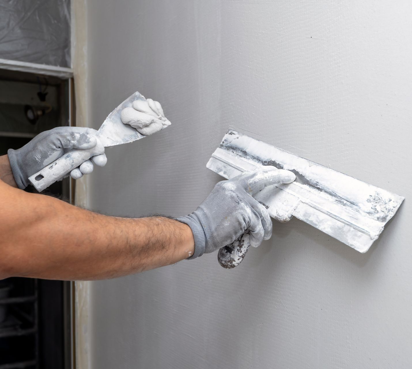 Un main applique de l'enduit sur un mur à l'aide d'un outil