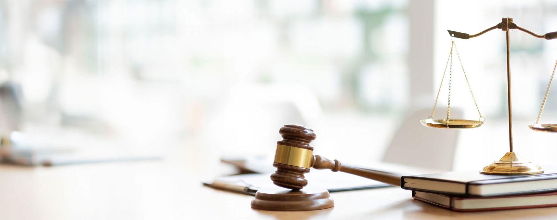Auf einem Tisch, der von einem Stapel Bücher bedeckt ist, stehen ein Hammer und eine Waage, die Recht und Gerechtigkeit symbolisieren.