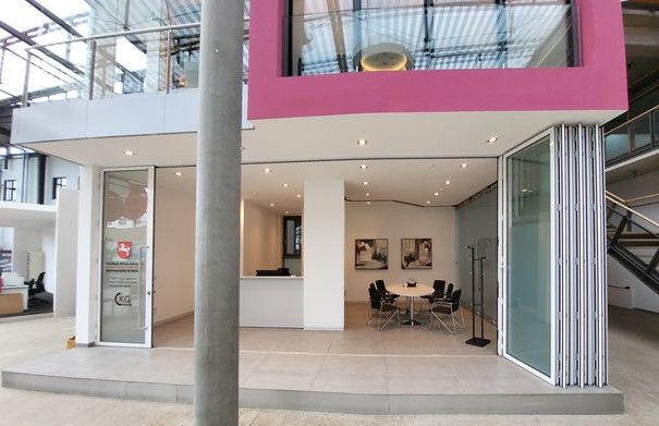 Modernes Bürogebäude mit rosa-weißer Fassade. Im Inneren befinden sich ein Besprechungsbereich, Kunstwerke und Falttüren aus Glas.