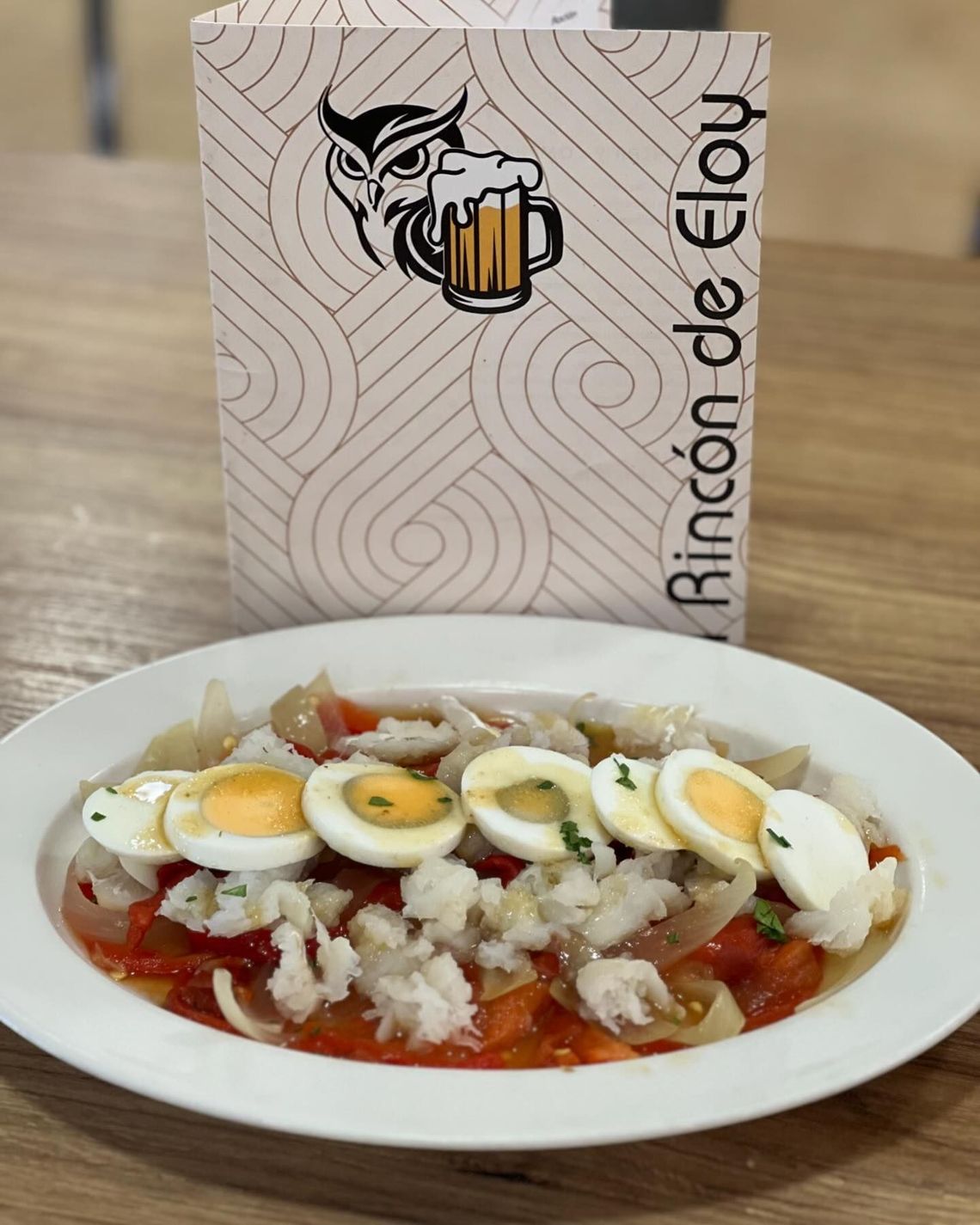 Plato de arroz con salsa roja, coronado con rodajas de huevo cocido, frente a un letrero de Rincón de Eloy.