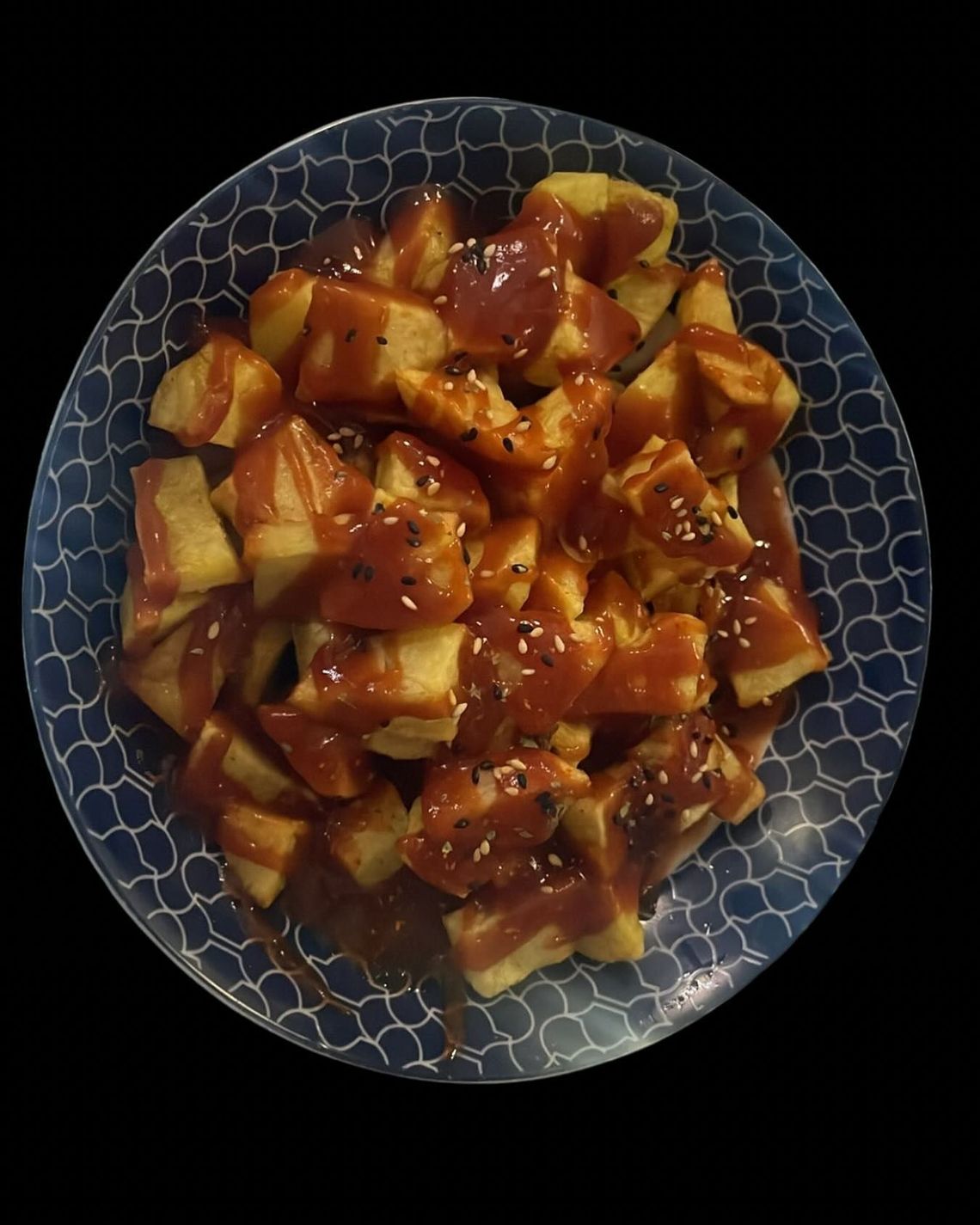 Bol azul con patatas cortadas en dados en salsa rojiza, adornado con hierbas.
