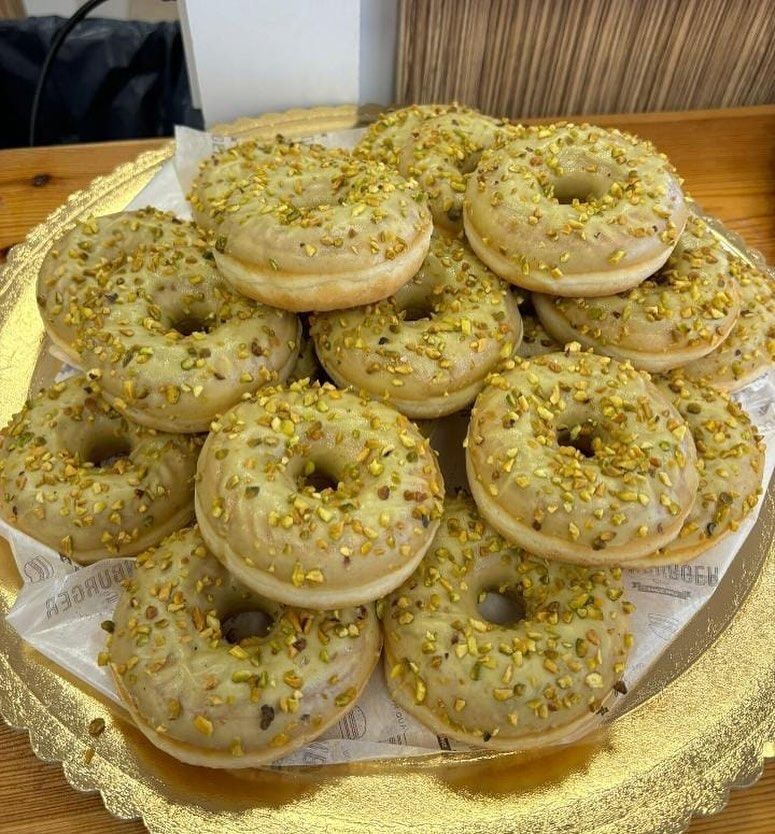Bandeja de donuts glaseados con pistachos sobre papel en el mostrador de una panadería.