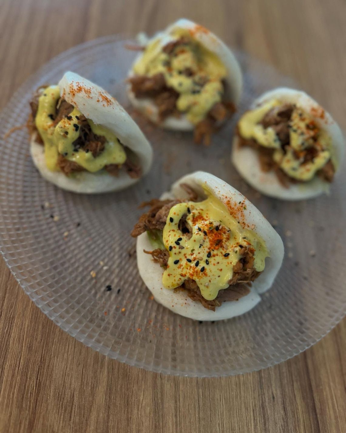 Cuatro empanadillas rellenas en un plato de cristal, cubiertas con un relleno cremoso y especias sobre una mesa de madera.
