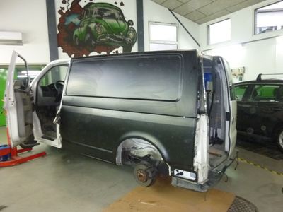 Ein Mechaniker in einem grauen Overall arbeitet in einer Werkstatt an der hinteren Stossstange eines Autos; das Auto ist blau.