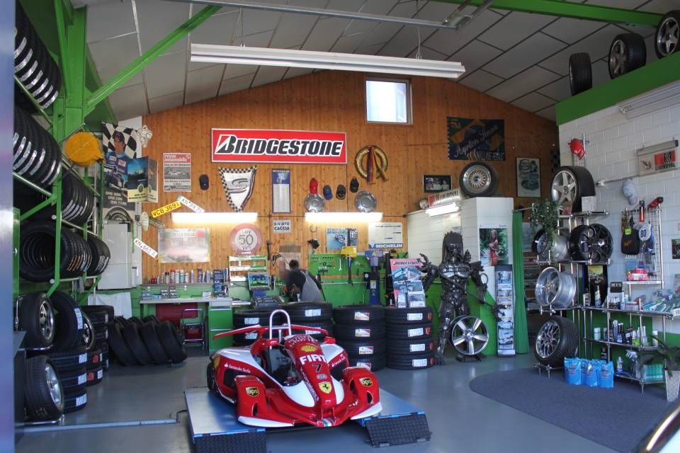 In einem Reifengeschäft steht ein roter Rennwagen auf einem Podest. Reifen und Autoteile sind an Wänden und in Regalen ausgestellt.