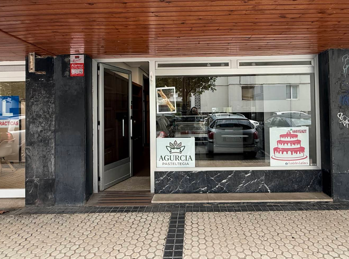 Fachada con escaparates, molduras de mármol negro y una acera embaldosada bajo un toldo de madera.