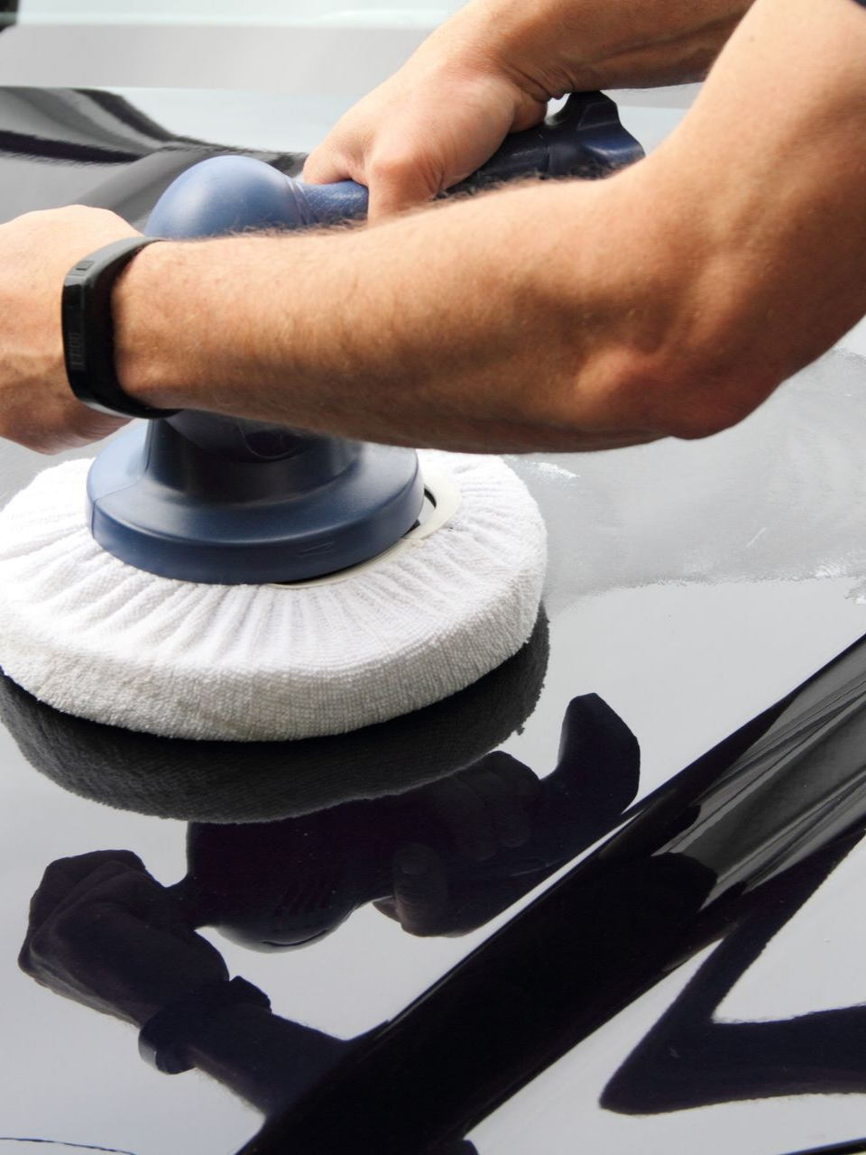 Personne polissant une voiture noire avec une polisseuse rotative, bras visibles.