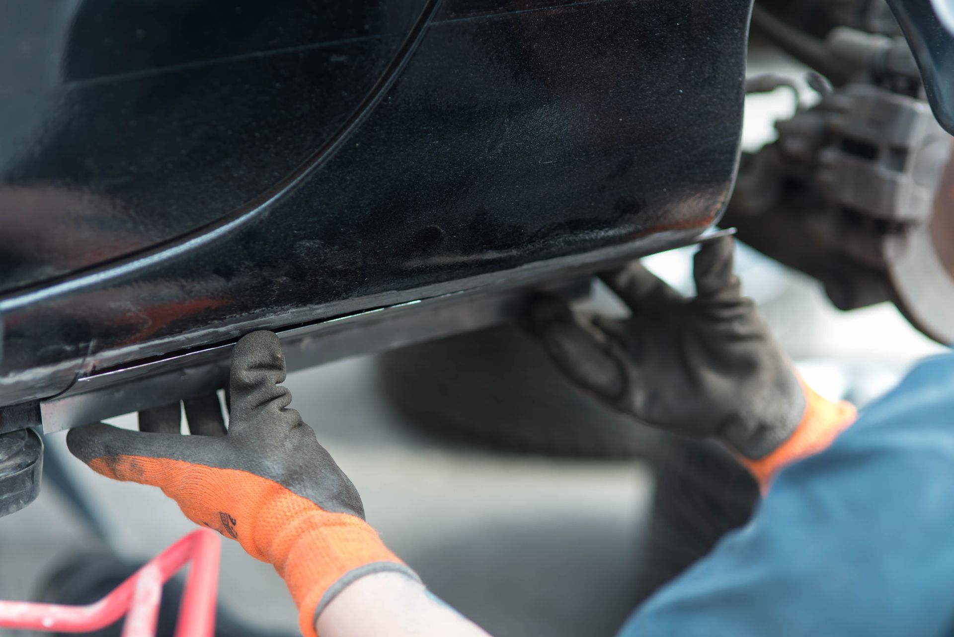 Une personne portant des gants orange répare le panneau latéral d'une voiture.