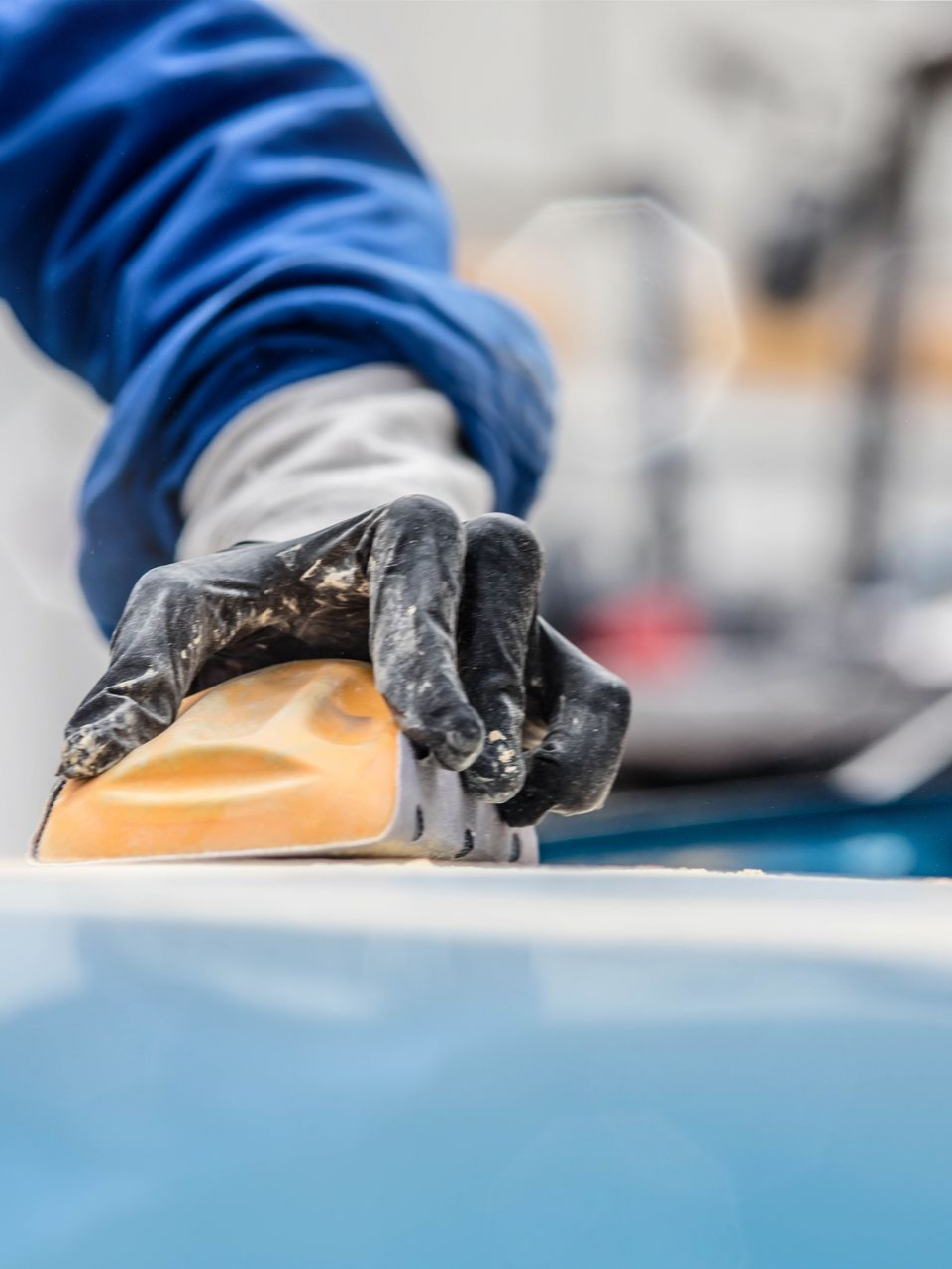 Main gantée d'une personne lissant une surface bleue avec un outil jaune, vêtue de vêtements de travail bleus.
