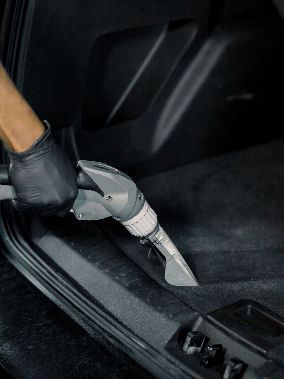 Main gantée utilisant un nettoyeur de tapis à l'intérieur d'une voiture ; nettoyage du tapis de sol de la voiture.