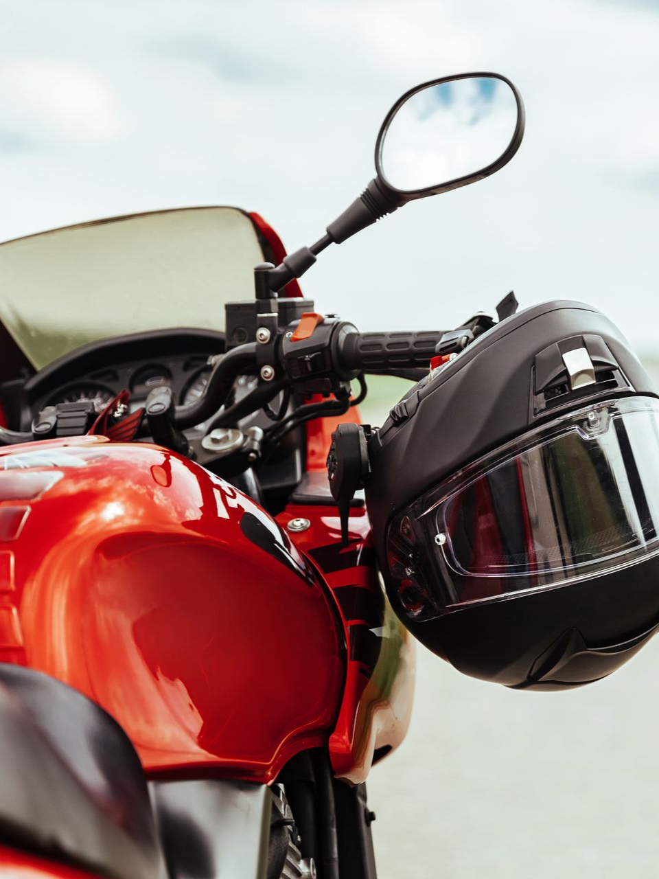 Une moto rouge avec un casque noir accroché au guidon.