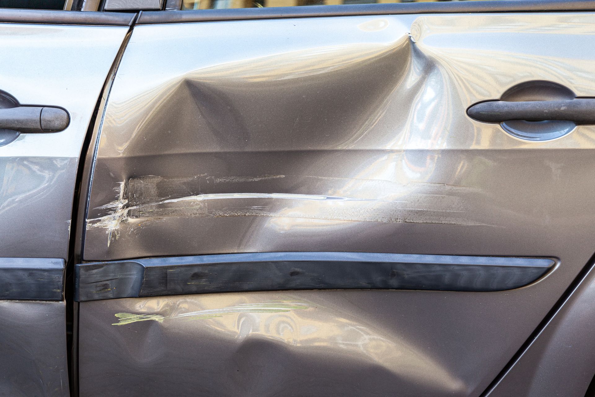 Portière de voiture grise endommagée, présentant une grosse bosse et des rayures.
