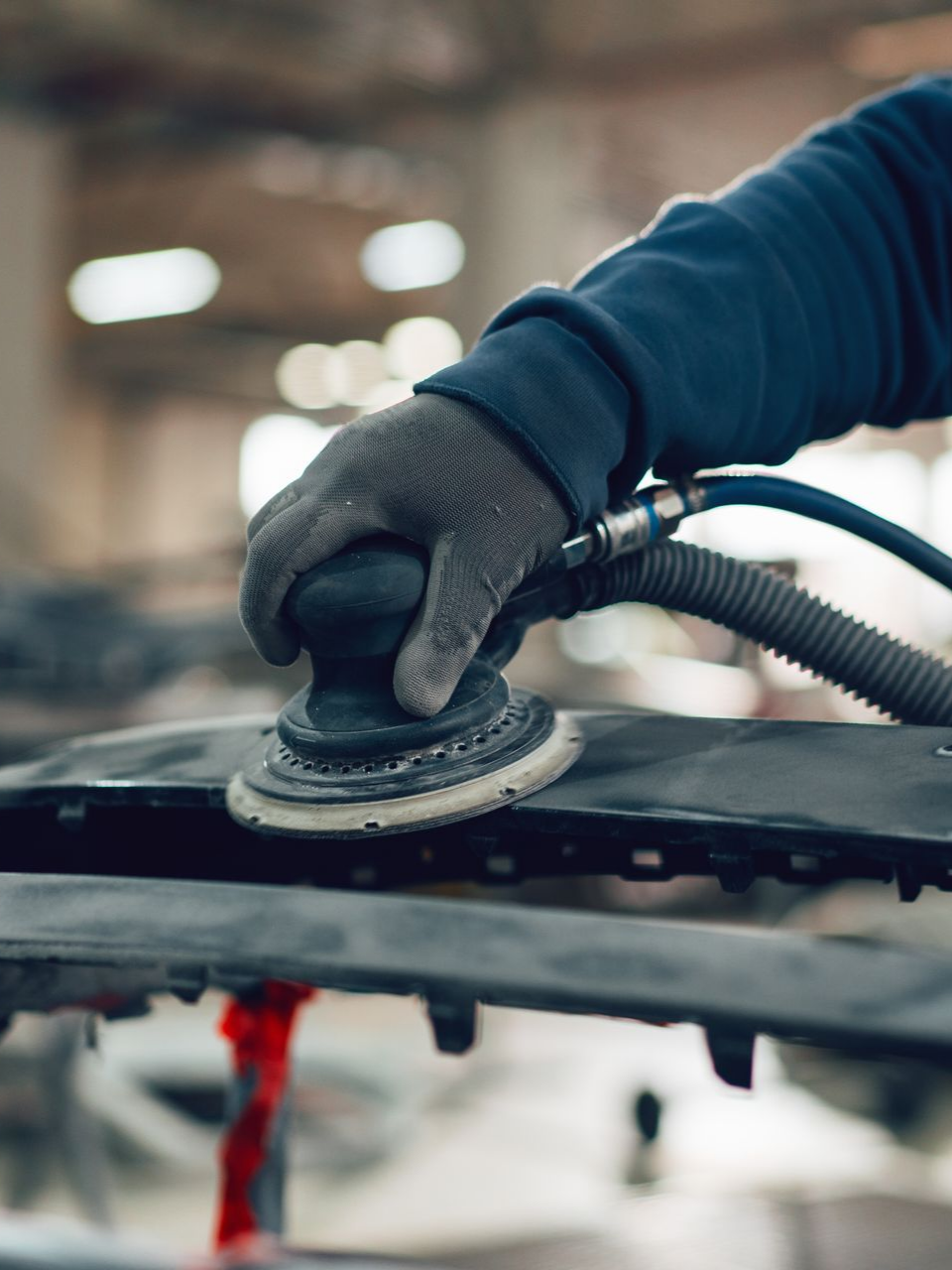 Main utilisant une ponceuse sur une pièce automobile dans un atelier.