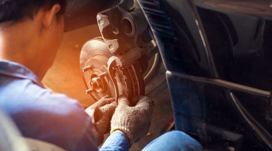 Manos enguantadas del mecánico sosteniendo un rotor de freno de automóvil, inspeccionando el disco y la pinza desgastados.