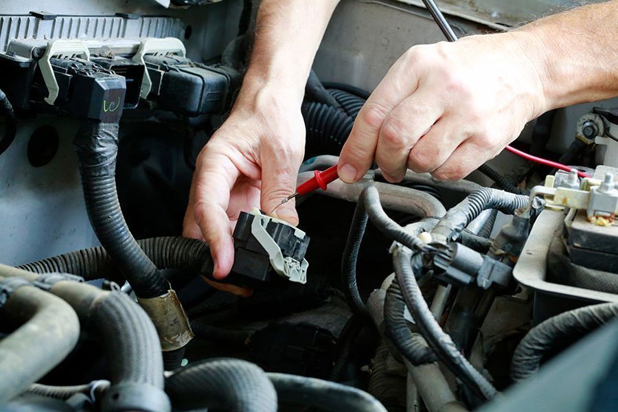 Manos utilizando un multímetro para probar un componente del motor de un automóvil.