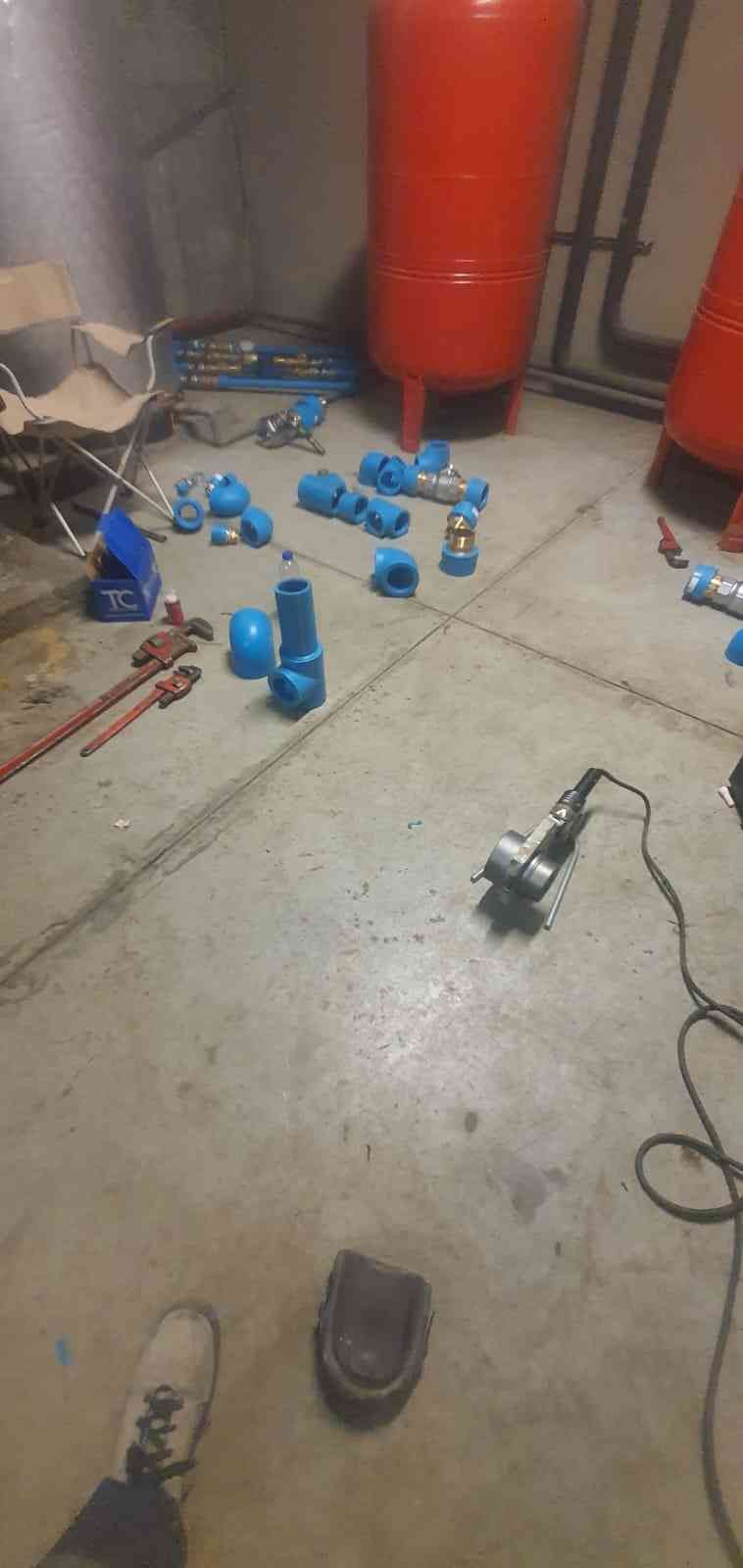 Un piso de taller lleno de suministros y herramientas de plomería, incluida una amoladora y varios accesorios de tubería azules.